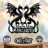 Black wedding cake topper with two winged dragons forming a heart-shaped opening, Mr and Mrs lettering, and the personalized surname SAUMENIG.