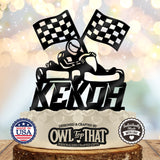 Black personalized name birthday cake topper featuring a helmeted go-kart driver beneath two checkered racing flags.