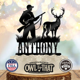 Black personalized cake topper featuring a hunter holding a scoped rifle beside an antlered buck, with grass details above the name.