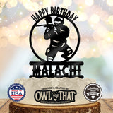 Black paintball birthday cake topper featuring a masked player crouching with a paintball marker inside a circular frame, with Happy Birthday and the name Malachi.