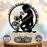 Black circular baby shower cake topper featuring an expectant mother holding a flower, wildflower details, and A Little Wildflower Is on the Way wording.