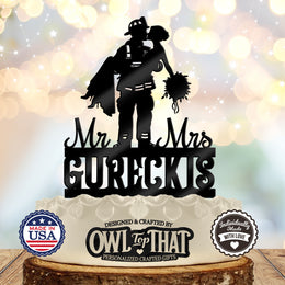 Black firefighter wedding cake topper featuring a firefighter carrying and kissing a bride holding a bouquet, with Mr and Mrs lettering and the surname GURECKIS.