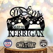 Black wedding cake topper with two game controllers, Mr and Mrs script, the date 06.07.26, and the personalized surname KERRIGAN.