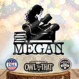 Black personalized MEGAN cake topper featuring a long-haired girl reading an open book in an armchair beside a stack of books.