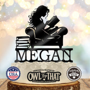Black personalized MEGAN cake topper featuring a long-haired girl reading an open book in an armchair beside a stack of books.