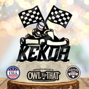 Black personalized name birthday cake topper featuring a helmeted go-kart driver beneath two checkered racing flags.