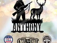 Black personalized cake topper featuring a hunter holding a scoped rifle beside an antlered buck, with grass details above the name.
