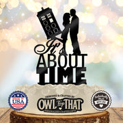 Black It’s About Time wedding cake topper featuring an embracing couple beside a tilted police call box time machine above stacked lettering.