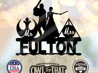 Black Jedi and wizard wedding cake topper with a lightsaber-wielding figure, wand-holding bride, Mr and Mrs emblems, and the personalized surname Fulton.