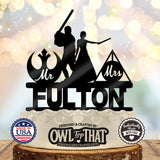 Black Jedi and wizard wedding cake topper with a lightsaber-wielding figure, wand-holding bride, Mr and Mrs emblems, and the personalized surname Fulton.