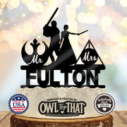 Black Jedi and wizard wedding cake topper with a lightsaber-wielding figure, wand-holding bride, Mr and Mrs emblems, and the personalized surname Fulton.