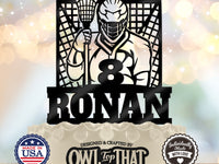 Black lacrosse birthday cake topper featuring a helmeted player holding a stick in front of a goal, personalized with the name Ronan and age 8.
