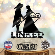 Black Link and Zelda wedding cake topper holding hands, with sword and shield details, the date 9.26.26 inside a heart, and LINKED lettering below.
