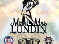 Black wedding cake topper featuring a uniformed sailor dipping his partner for a kiss above Mr and Mrs lettering and the personalized surname LUNDIN.