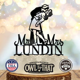 Black wedding cake topper featuring a uniformed sailor dipping his partner for a kiss above Mr and Mrs lettering and the personalized surname LUNDIN.