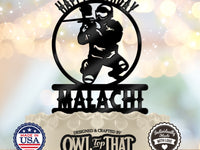 Black paintball birthday cake topper featuring a masked player crouching with a paintball marker inside a circular frame, with Happy Birthday and the name Malachi.