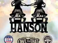 Black snowmobile wedding cake topper featuring two helmeted riders fist-bumping on Mr and Mrs snowmobiles above the personalized surname Hanson.