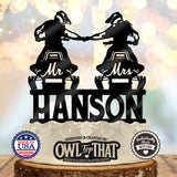 Black snowmobile wedding cake topper featuring two helmeted riders fist-bumping on Mr and Mrs snowmobiles above the personalized surname Hanson.