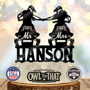 Black snowmobile wedding cake topper featuring two helmeted riders fist-bumping on Mr and Mrs snowmobiles above the personalized surname Hanson.