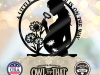 Black circular baby shower cake topper featuring an expectant mother holding a flower, wildflower details, and A Little Wildflower Is on the Way wording.