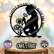 Black circular baby shower cake topper featuring an expectant mother holding a flower, wildflower details, and A Little Wildflower Is on the Way wording.